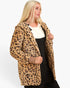 A blonde woman wearing a leopard print fuzzy hooded jacket over a black and white top, photographed against a plain light gray studio background.