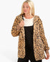 A blonde woman wearing a plush leopard-print hooded jacket over a black dress and white sweater, photographed against a plain white studio background.