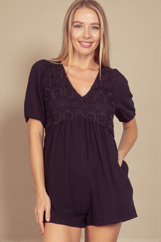 Woman wearing a black romper with lace details on a beige background