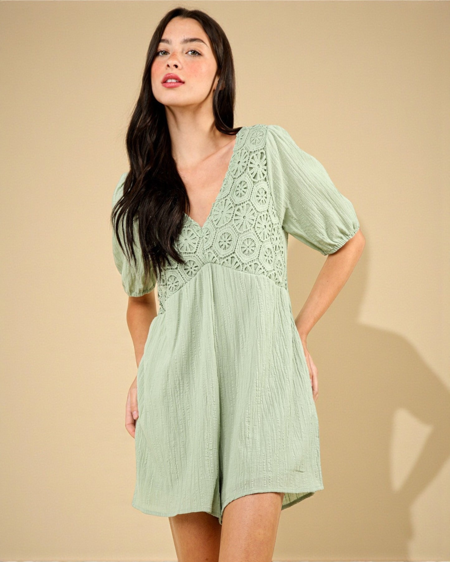 Woman wearing a light green dress with lace details against a beige background