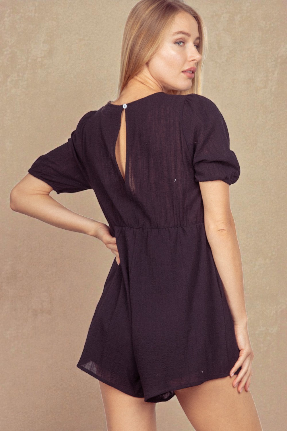 Woman wearing a black romper with open back on a beige background