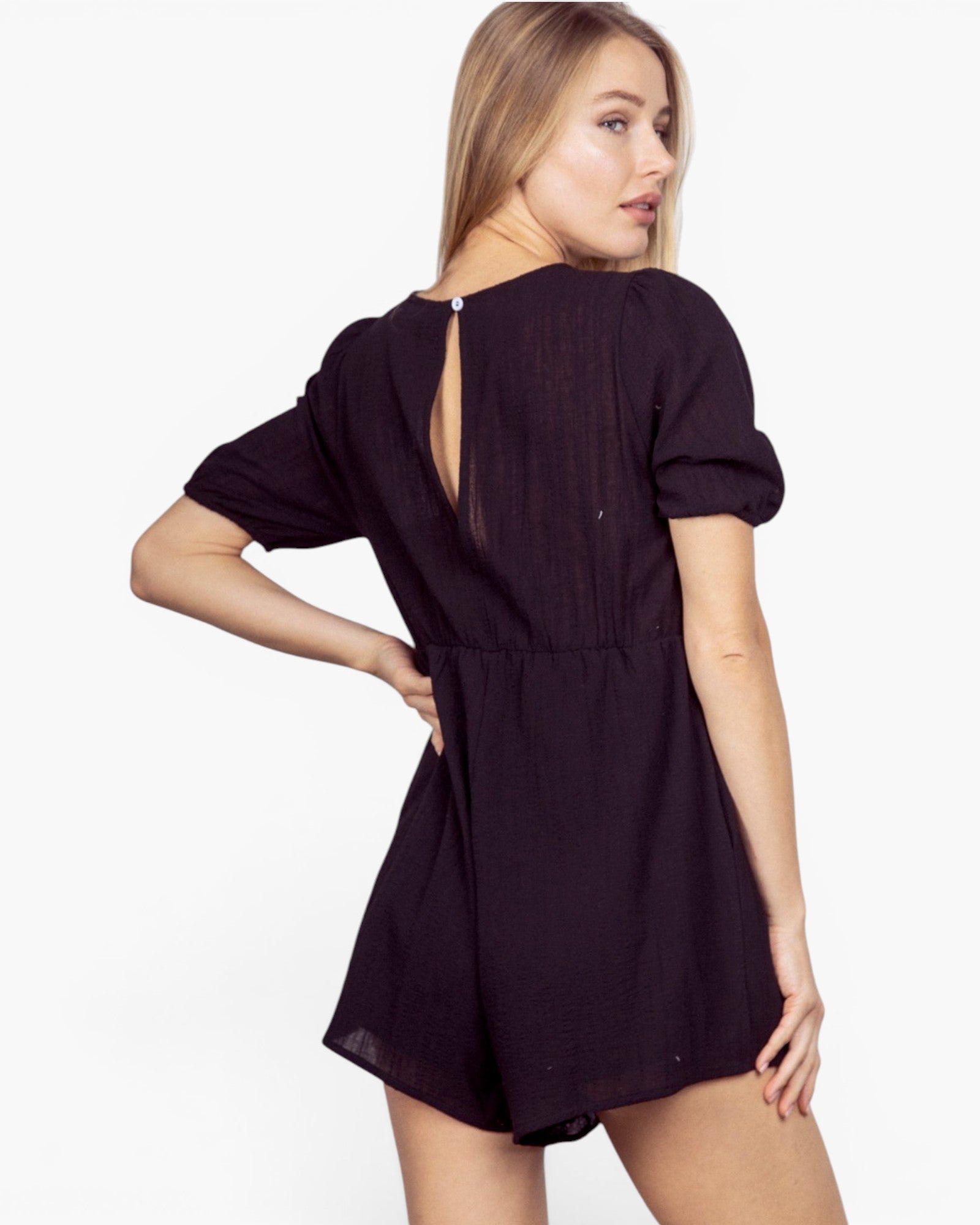 A woman modeling a short-sleeve black romper from the back, showing a keyhole back closure, against a plain white studio background.