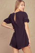 Woman wearing a black romper with open back on a beige background