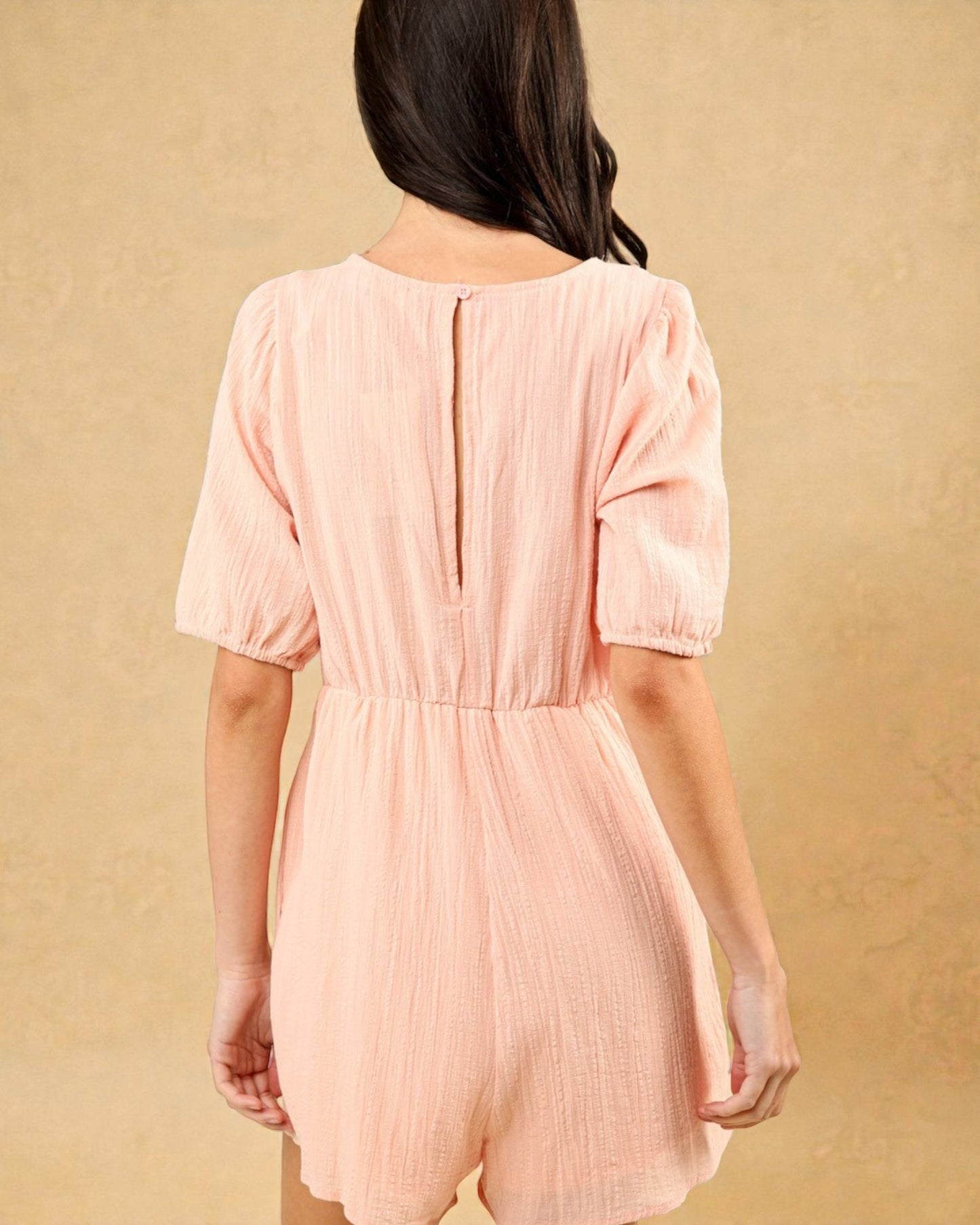 Person wearing a pink romper against a beige background