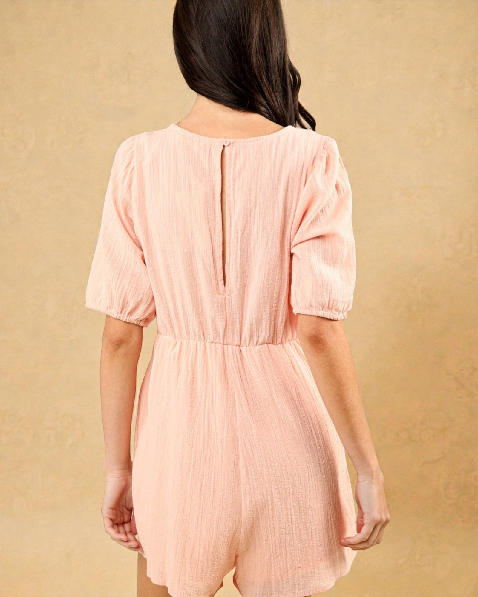 Person wearing a pink romper against a beige background