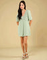 Woman wearing a light green dress with lace details on a beige background