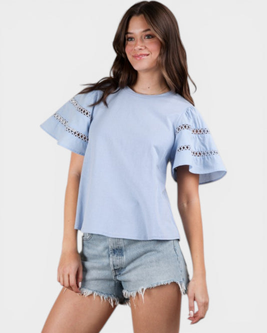 Woman wearing a light blue top with lace details and denim shorts on a white background