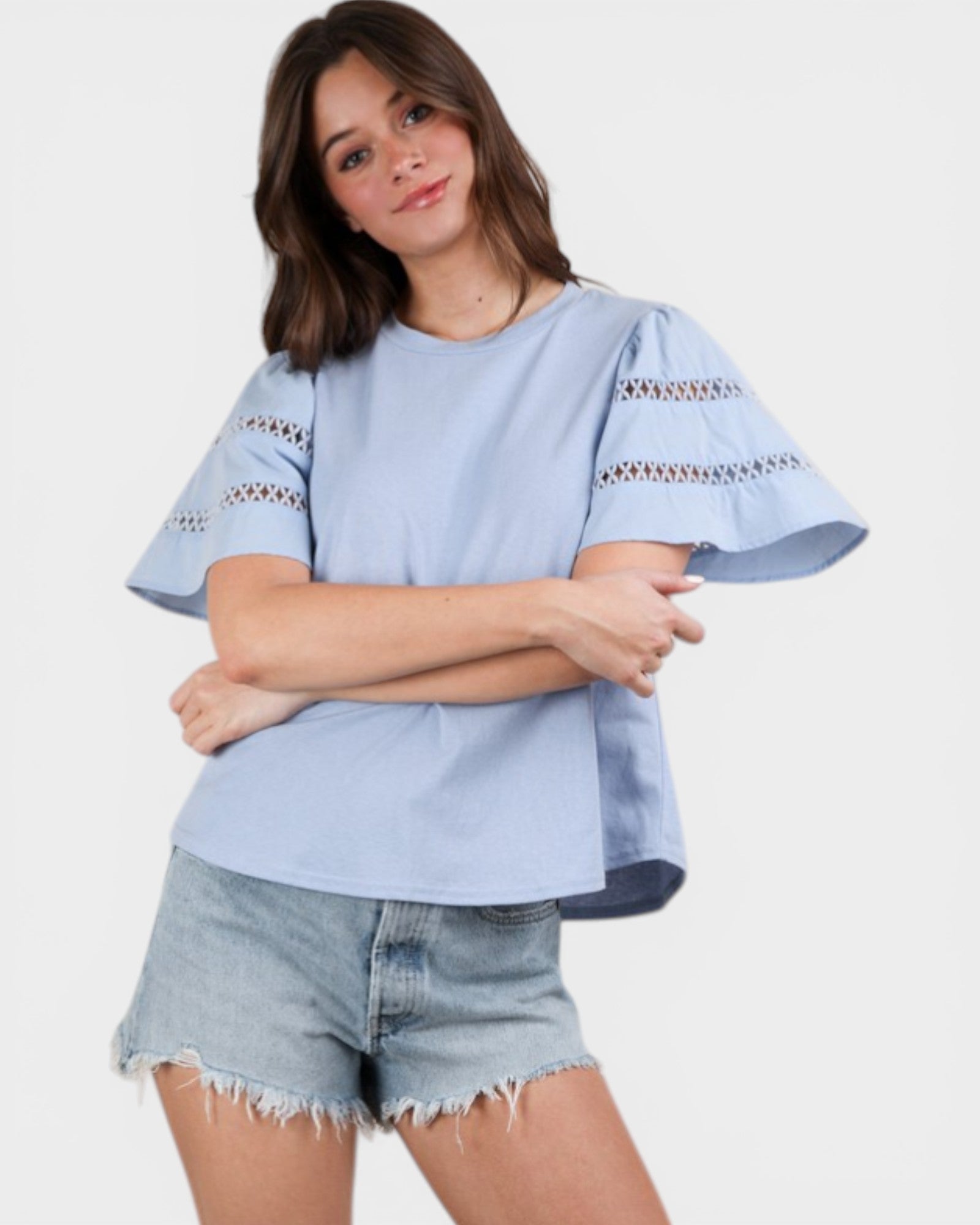 Woman wearing a light blue blouse with lace details and denim shorts on a white background