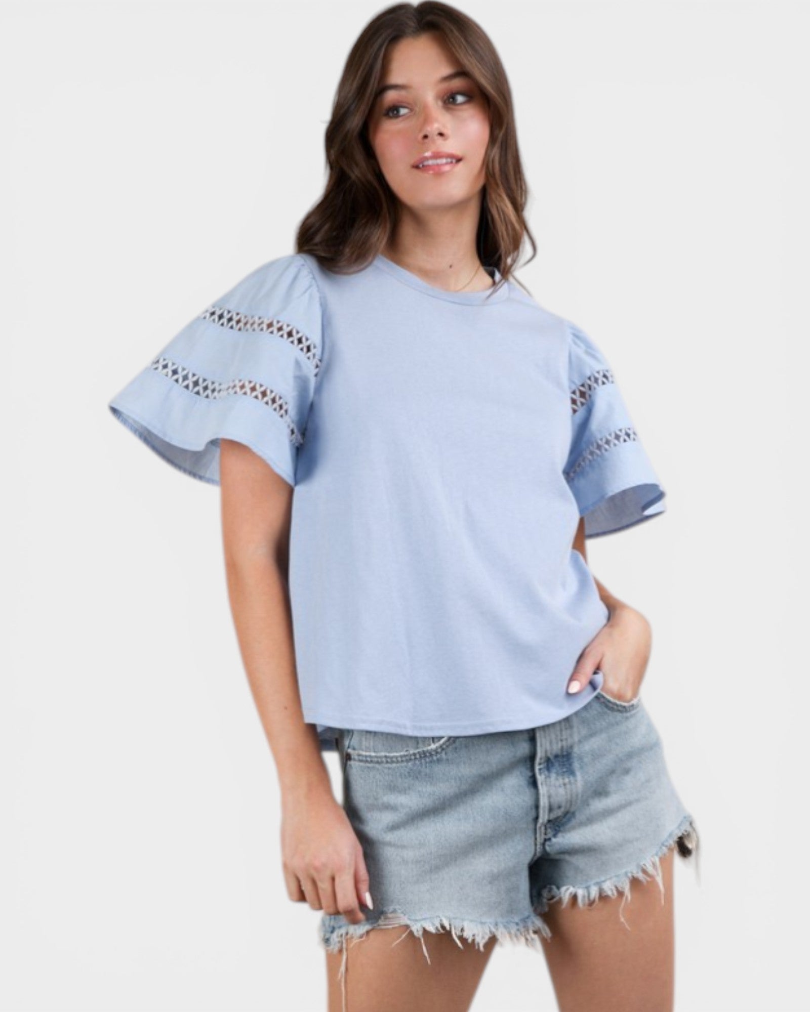 Woman wearing a light blue top with lace details and denim shorts on a white background