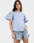 Woman wearing a light blue top with lace details and denim shorts on a white background