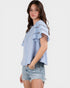 Woman wearing a light blue blouse with ruffled sleeves and denim shorts on a white background