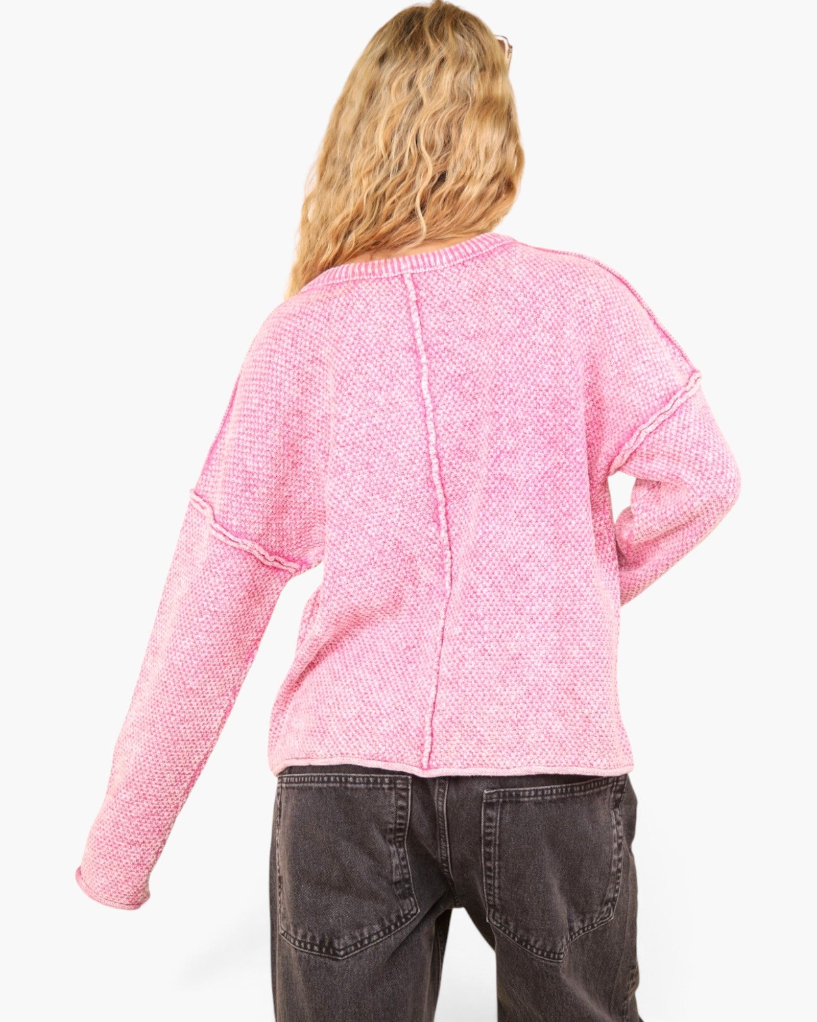 A woman shown from the back wearing a pink textured knit cardigan and dark gray jeans against a plain white background.