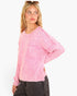 A woman wearing a pink textured knit sweater with a chest pocket, paired with dark gray jeans, photographed against a clean white background.