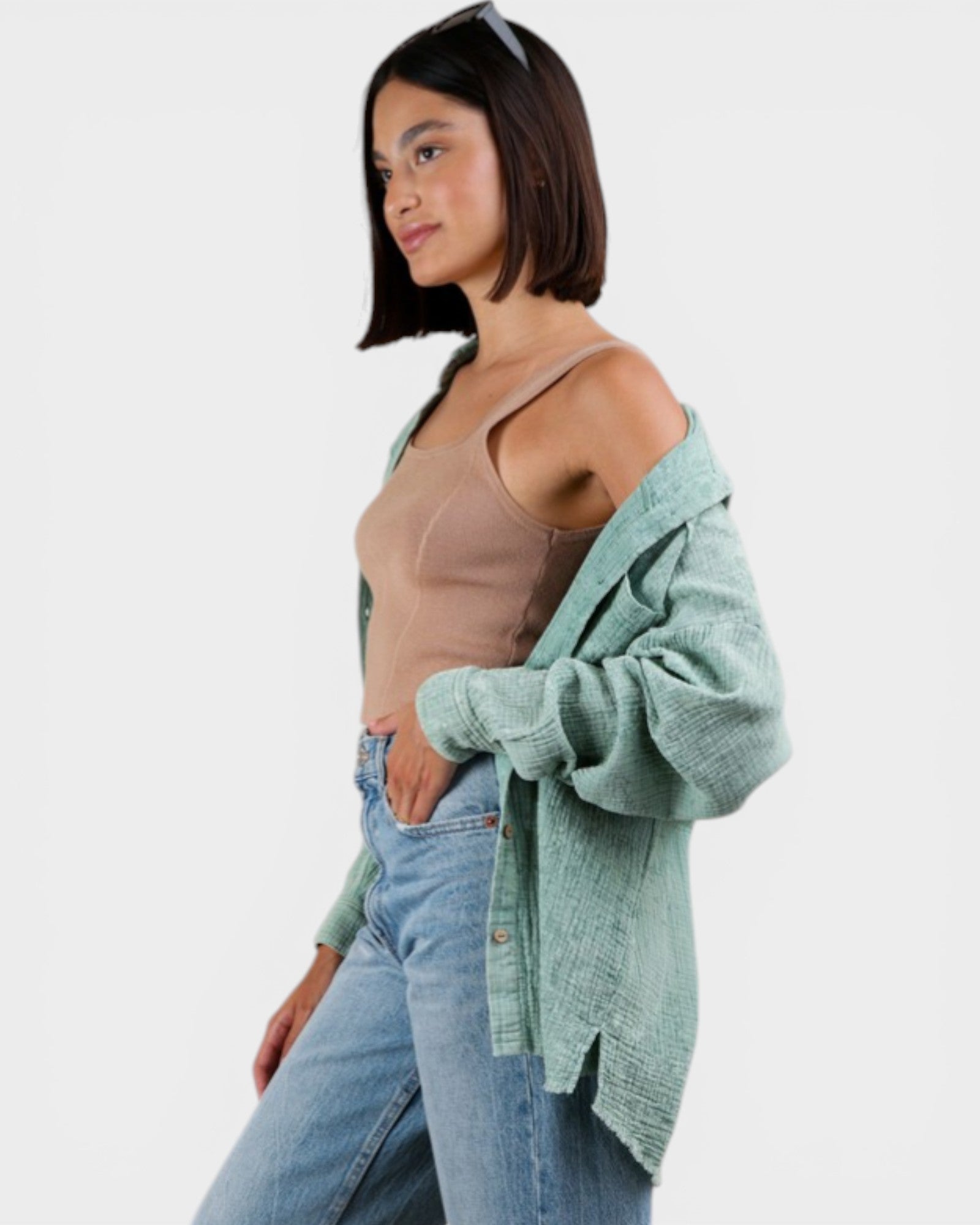 Woman wearing a light green cardigan over a beige top and blue jeans on a white background