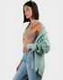 Woman wearing a light green cardigan over a beige top and blue jeans on a white background