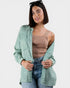 Woman wearing a light green jacket over a beige top and blue jeans on a white background