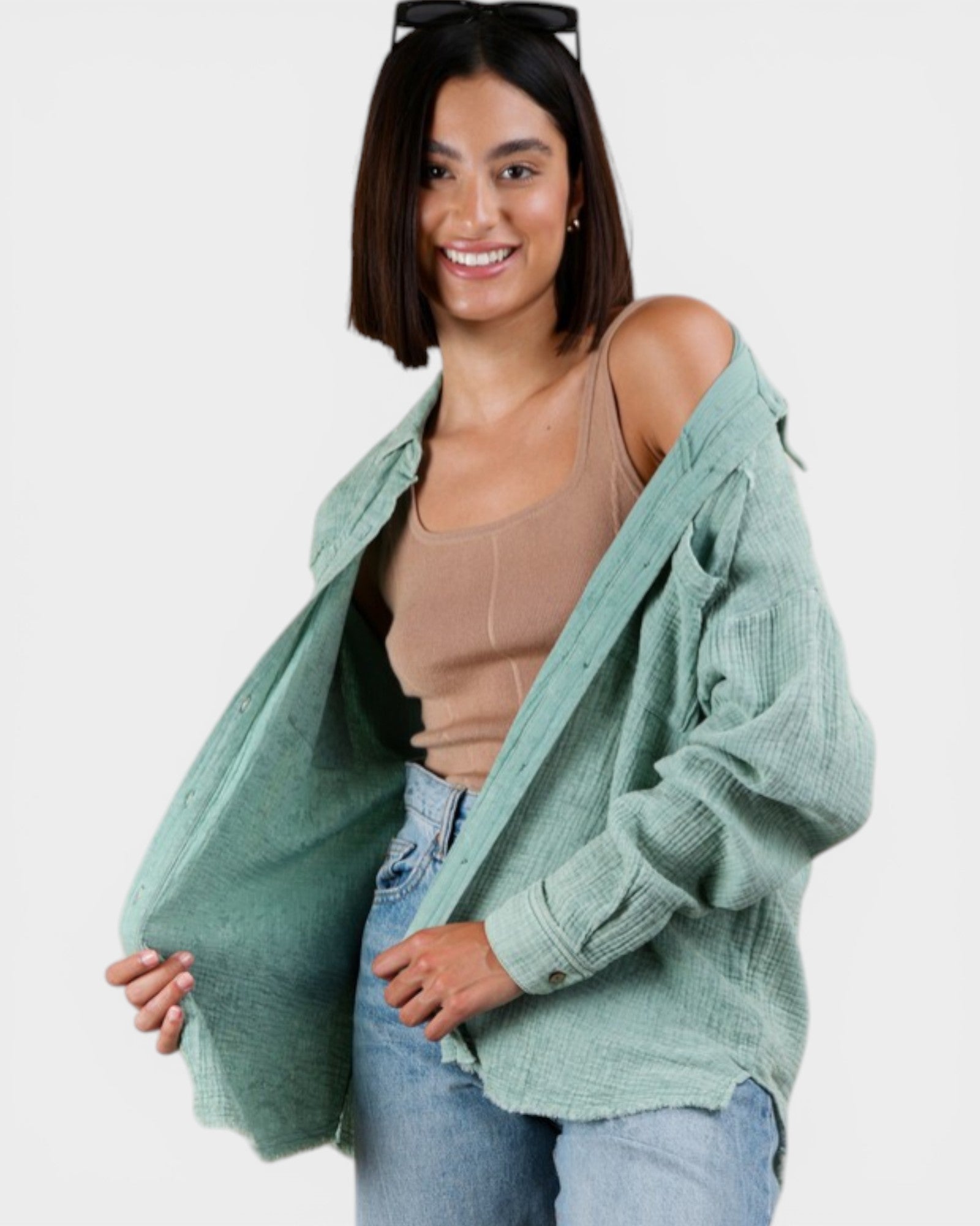 Woman wearing a light green cardigan over a beige top and blue jeans on a white background