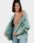 Woman wearing a light green cardigan over a beige top and blue jeans on a white background