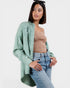 Woman wearing a light green cardigan, beige top, and blue jeans on a white background