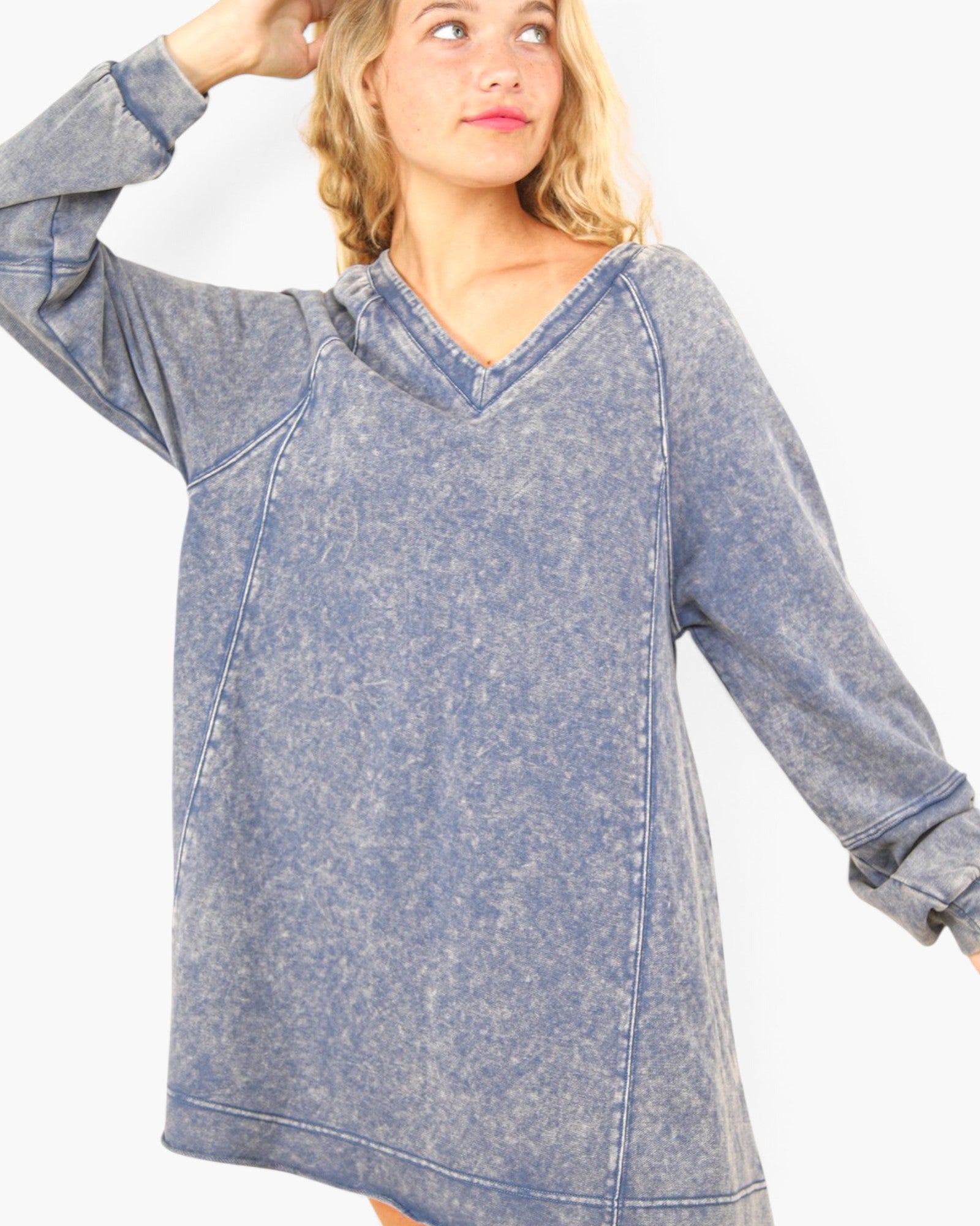 A woman wearing a long-sleeve, oversized V-neck top with a washed, acid-wash blue denim-like texture, shown against a plain light background.