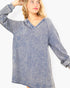 A woman wearing a long-sleeve, oversized V-neck top with a washed, acid-wash blue denim-like texture, shown against a plain light background.