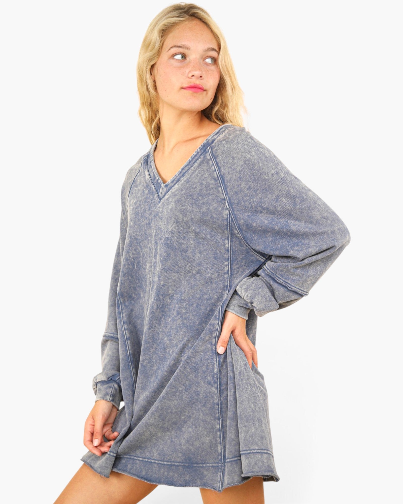 A woman modeling a washed, oversized blue-gray long-sleeve tunic dress with a V-neck and voluminous sleeves against a plain white background.