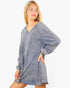 A woman modeling a washed, oversized blue-gray long-sleeve tunic dress with a V-neck and voluminous sleeves against a plain white background.