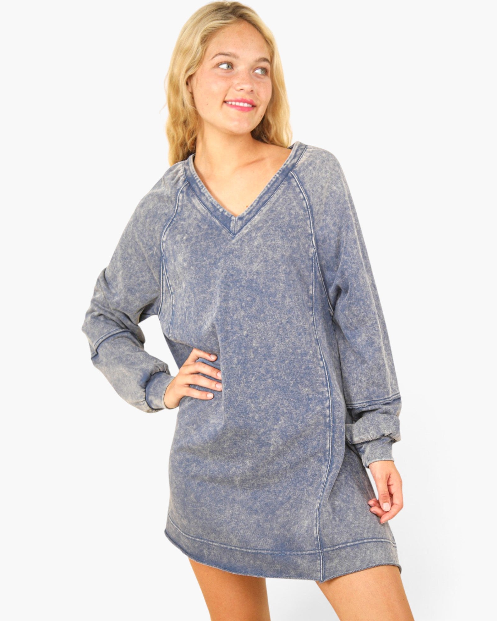 A woman modeling a long-sleeve, V-neck mini sweatshirt dress in a washed slate blue color, set against a plain white studio background.