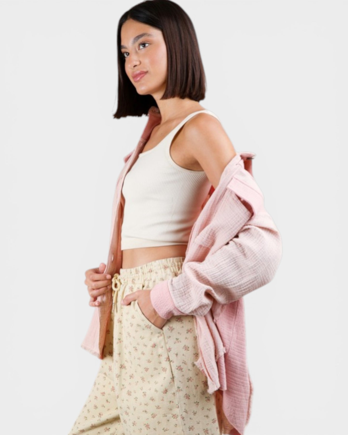 Woman wearing a white tank top and light-colored pants with a pink cardigan on a plain background