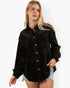 A woman modeling a black long-sleeve button-front shirt jacket made of textured corduroy or velvety fabric, paired with light denim shorts, against a plain white studio background.