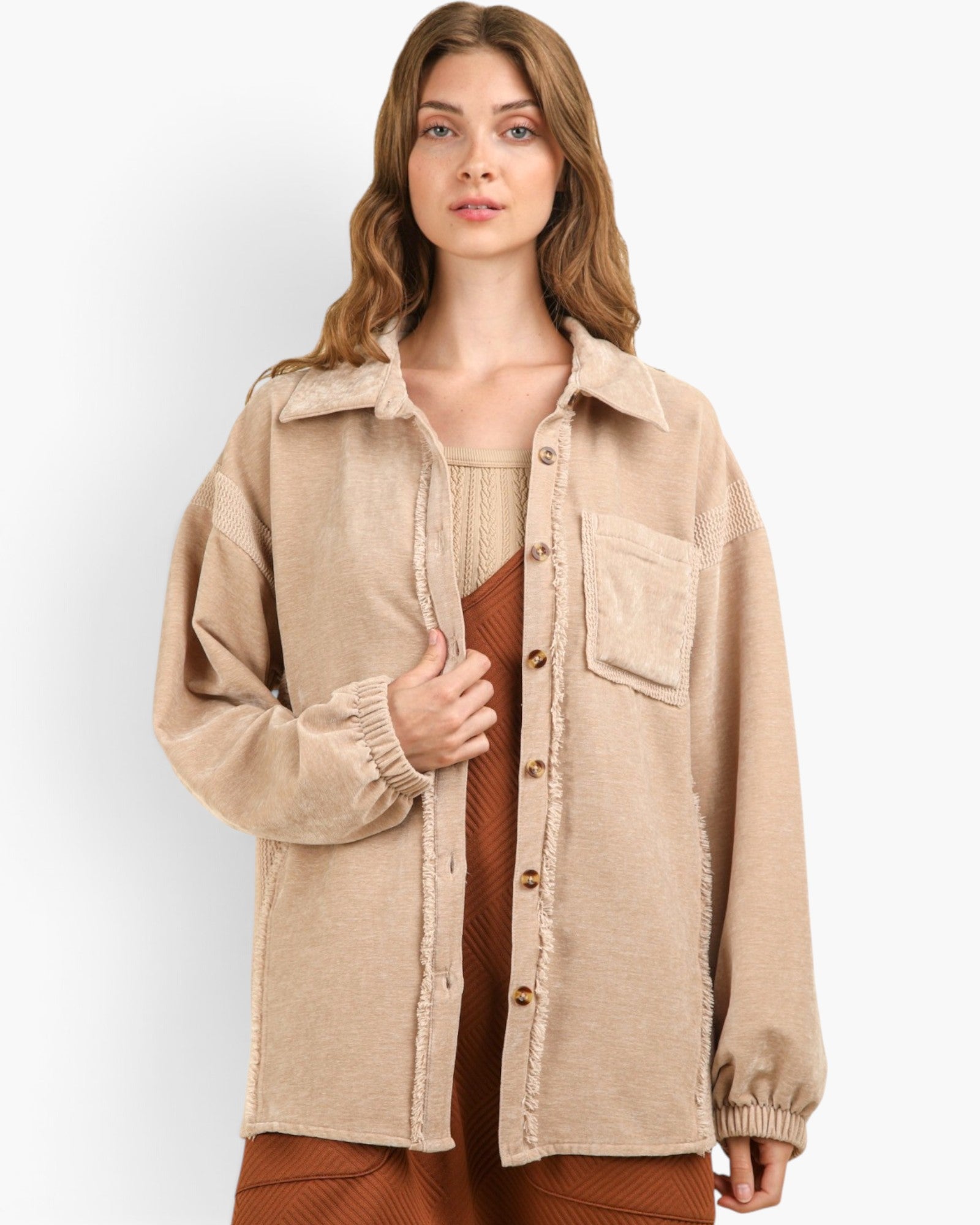 A woman wearing a beige corduroy button-up overshirt with raw-edge detailing over a rust-brown ribbed top and matching bottoms, photographed against a clean light gray studio background.