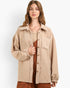 A woman wearing a beige corduroy button-up overshirt with raw-edge detailing over a rust-brown ribbed top and matching bottoms, photographed against a clean light gray studio background.