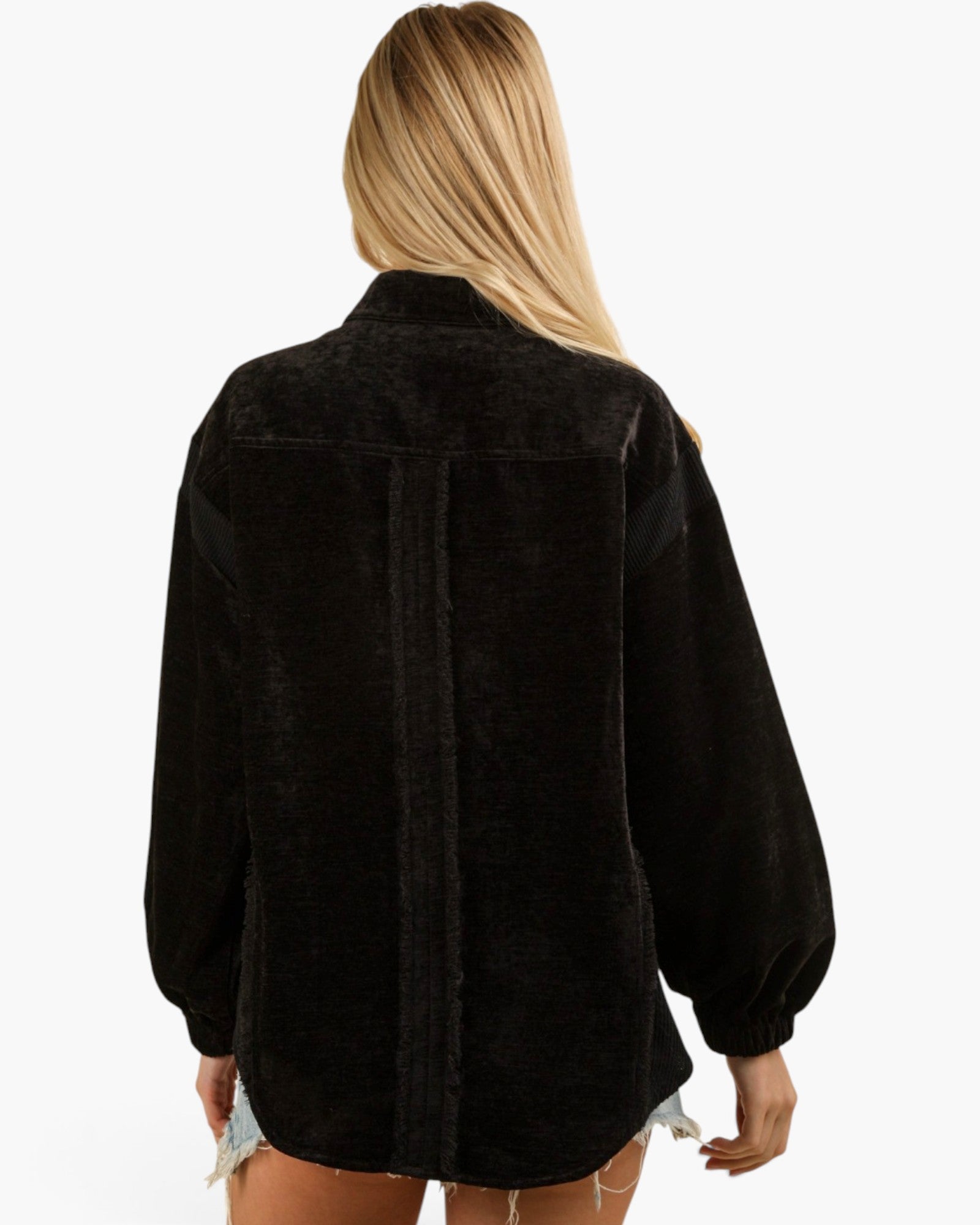 A woman viewed from the back wearing a black textured long-sleeve shirt jacket, set against a plain white background.