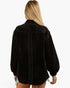 A woman viewed from the back wearing a black textured long-sleeve shirt jacket, set against a plain white background.