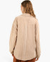 A woman shown from the back wearing a beige textured long-sleeve shirt jacket with a vertical seam detail on the back, set against a plain white background.