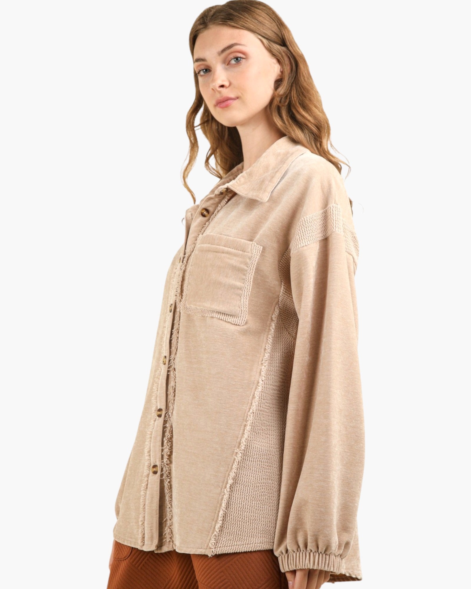 A woman wearing a beige textured button-up shirt jacket with knit side panels and elastic cuffs, photographed against a plain light gray studio background.