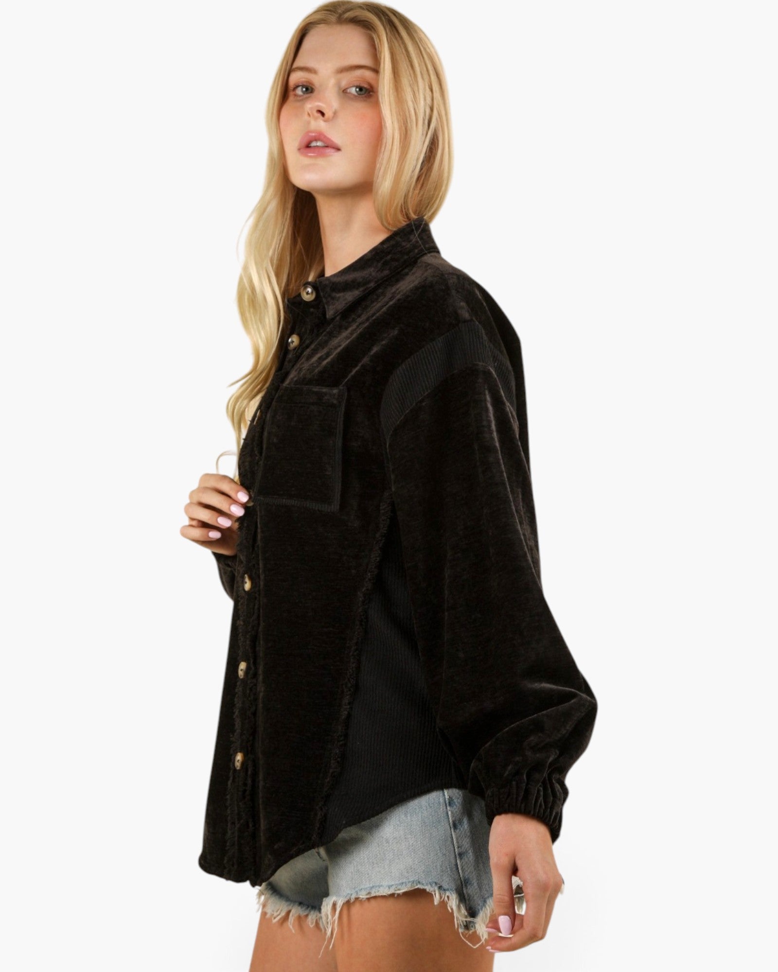 A woman modeling a black corduroy button-up shirt jacket with a chest pocket, paired with denim shorts, against a plain white background.