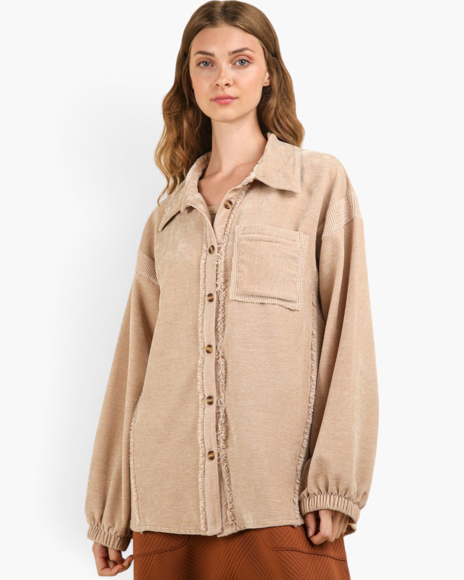 A woman wearing a beige button-up shirt jacket with textured fringe trim and elastic cuffs, paired with brown pants, against a plain white studio background.