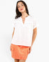 A woman modeling a white short-sleeve top with a split neckline and ruffle details, paired with an orange mini skirt, against a plain white studio background.