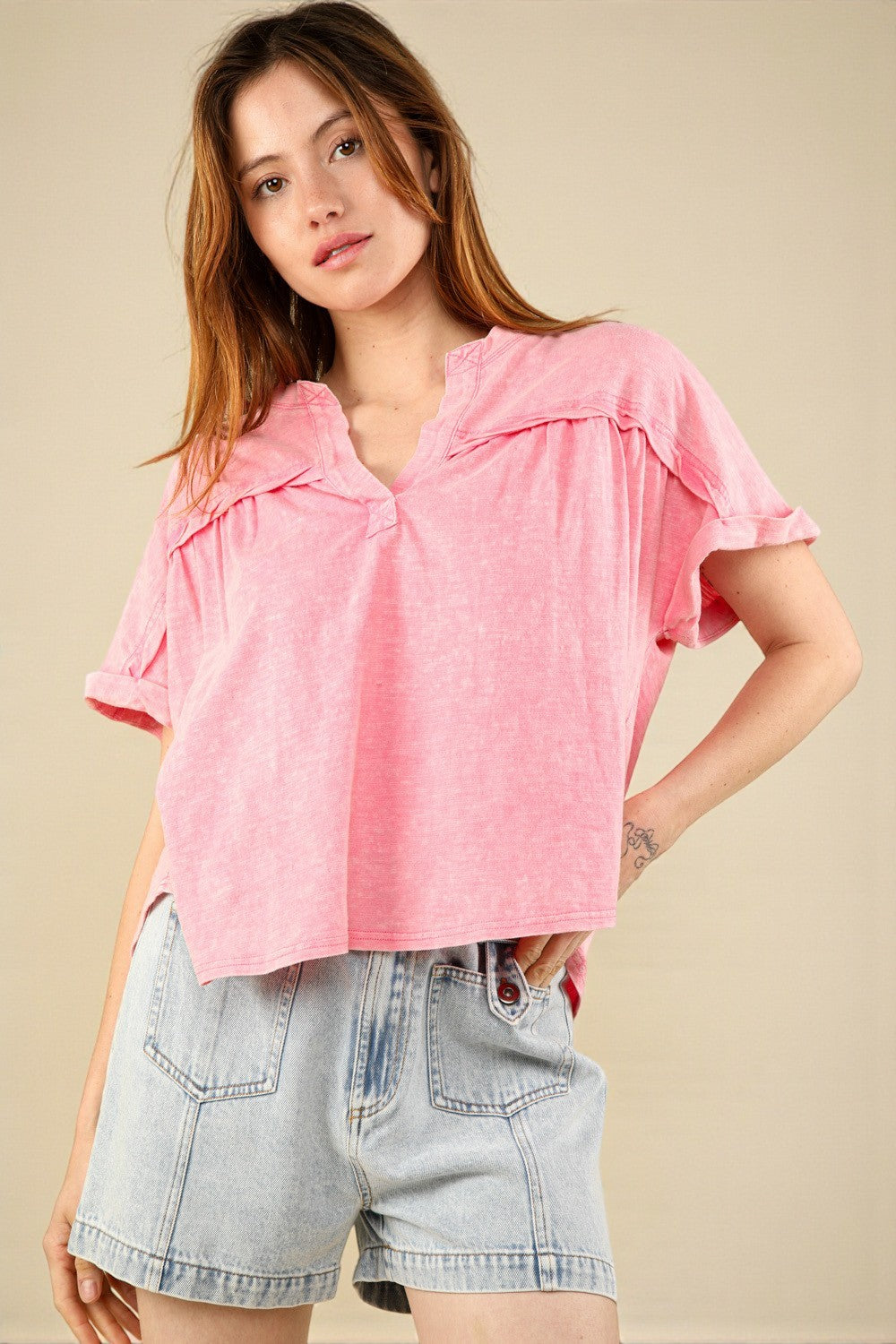Woman wearing a pink top and denim shorts on a beige background