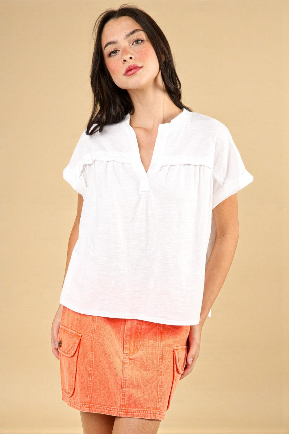 Woman wearing a white blouse and orange skirt against a beige background