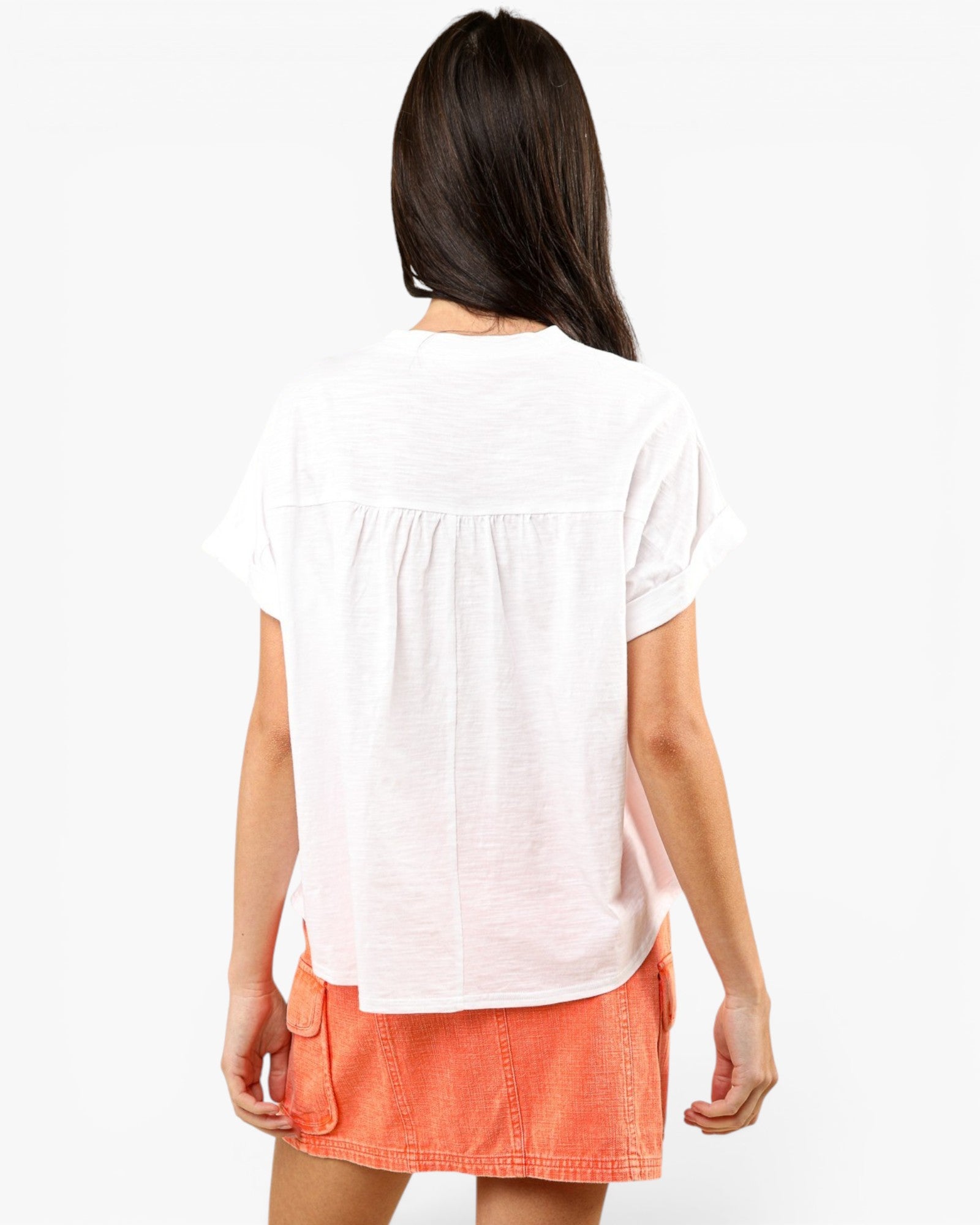 A woman shown from the back wearing a white short-sleeve top with a gathered back seam and an orange skirt, against a plain white background.