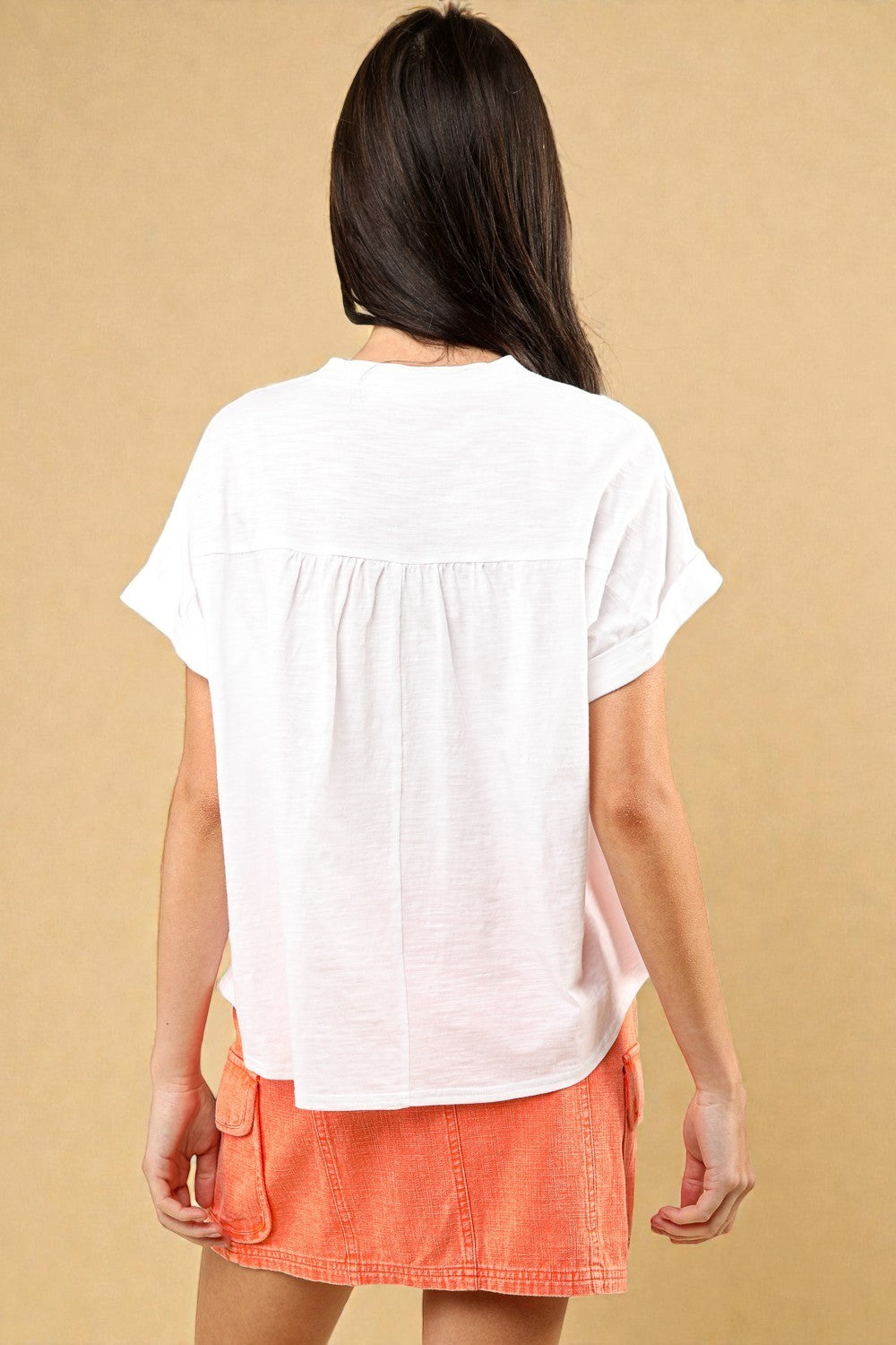 Woman wearing a white top and orange skirt against a beige background
