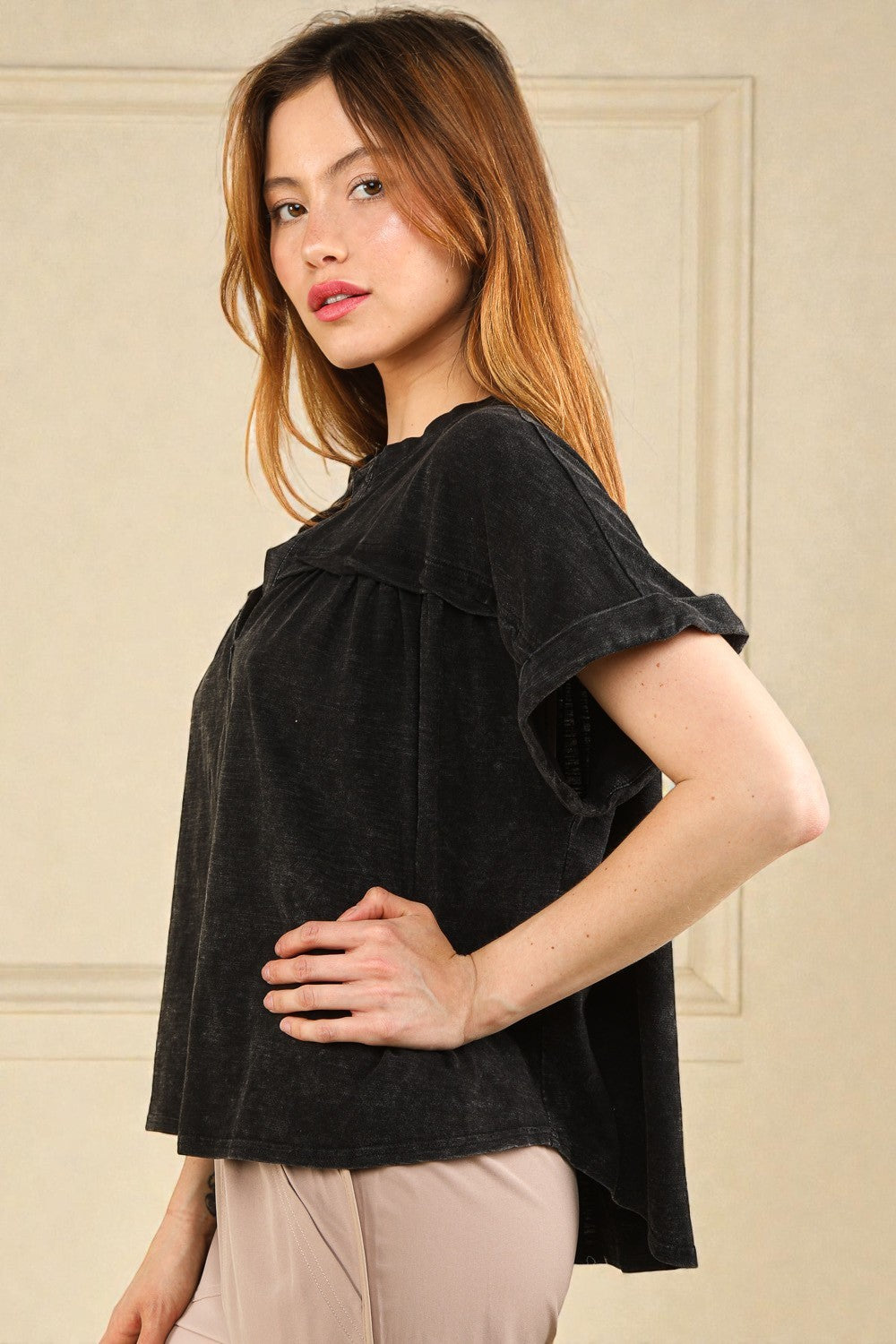 Woman wearing a black top with ruffled shoulders against a beige wall.