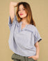 Woman wearing a light blue blouse with ruffled details against a beige background