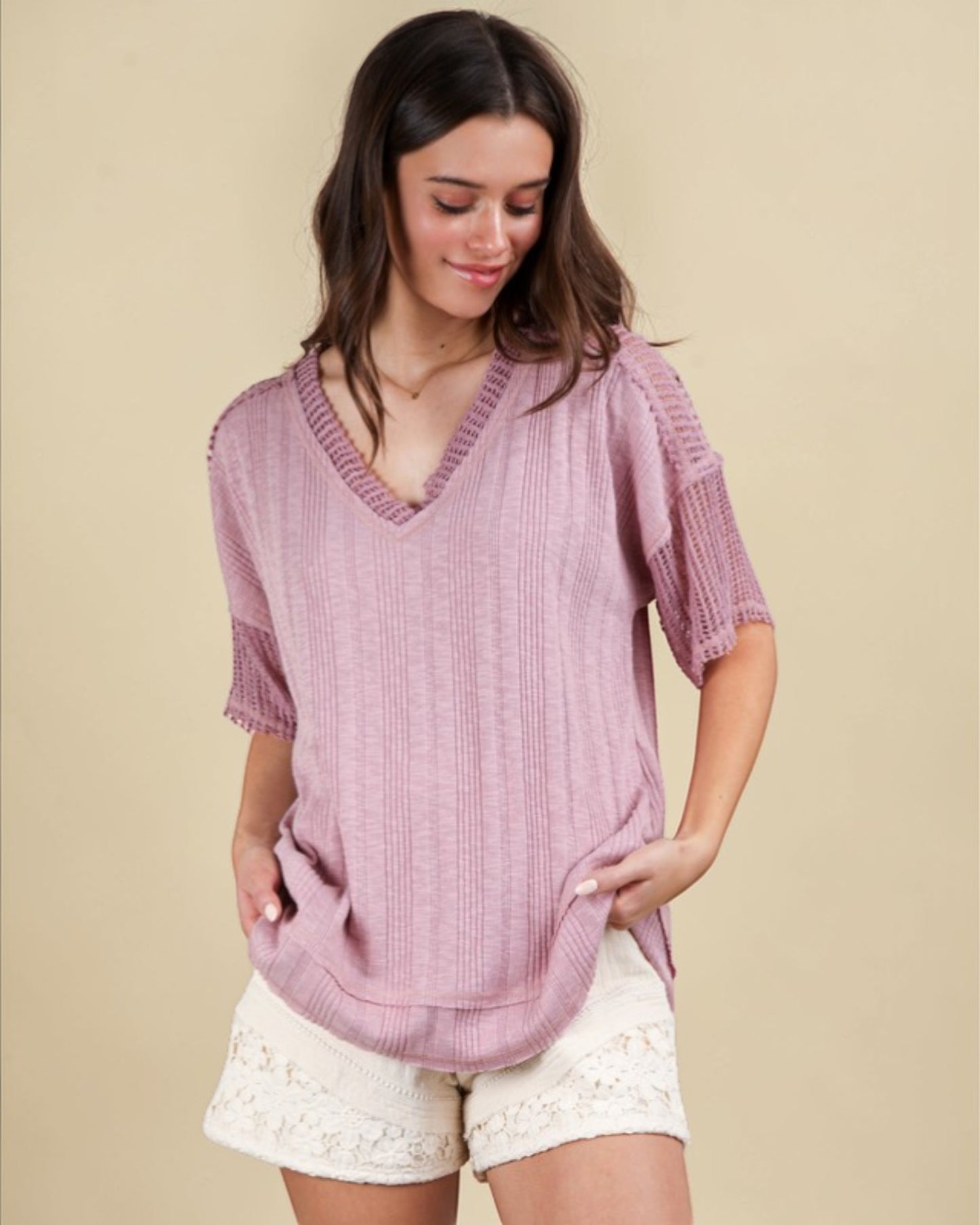 Woman wearing a pink knitted top and white shorts on a beige background