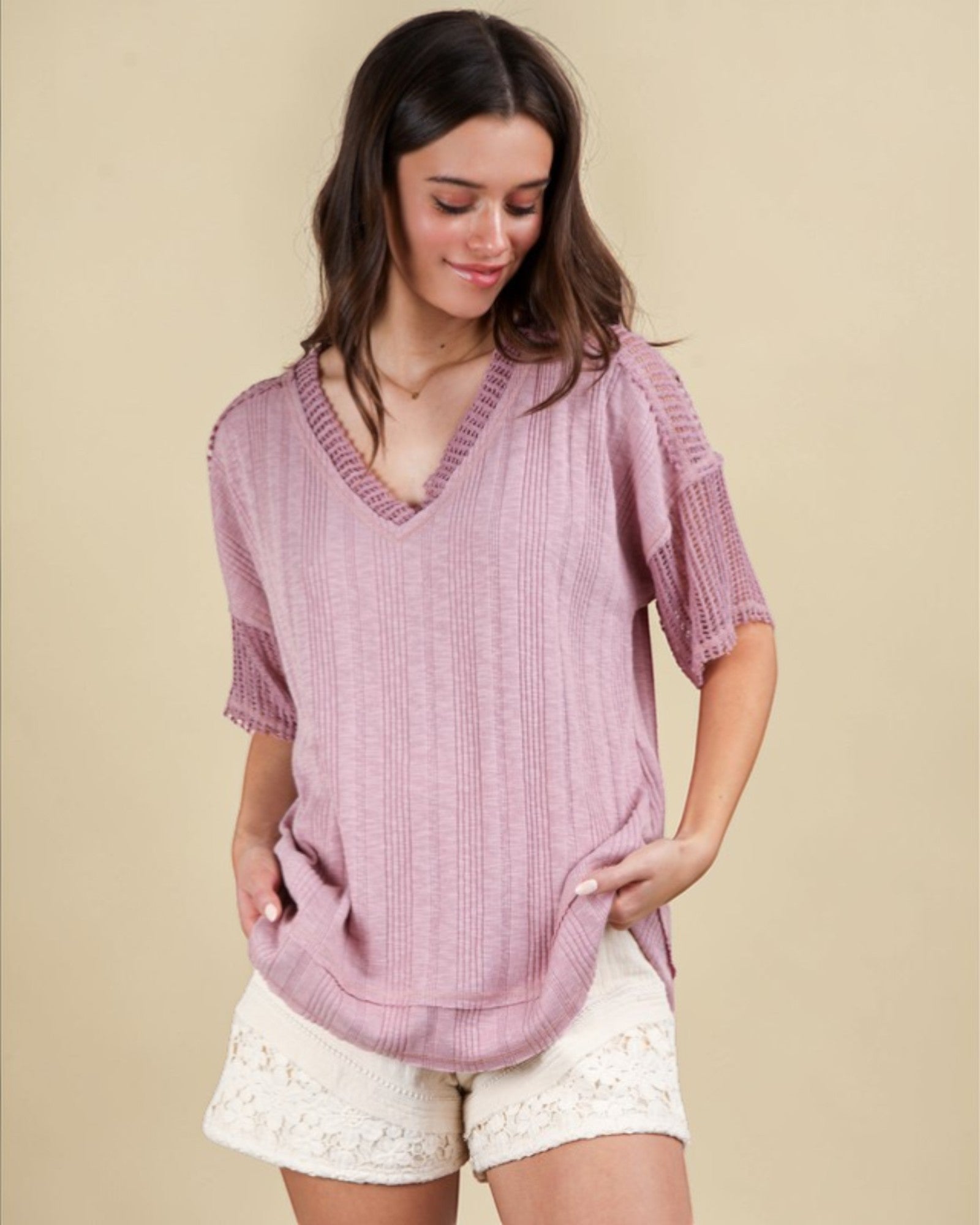 Woman wearing a pink knitted top and white shorts on a beige background