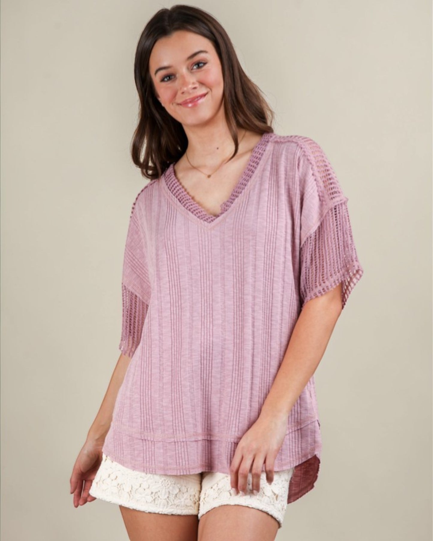 Woman wearing a pink textured top and white shorts on a beige background