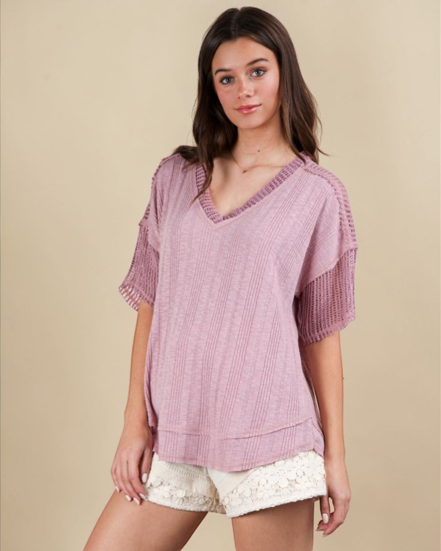 Woman wearing a pink textured top and white shorts on a beige background