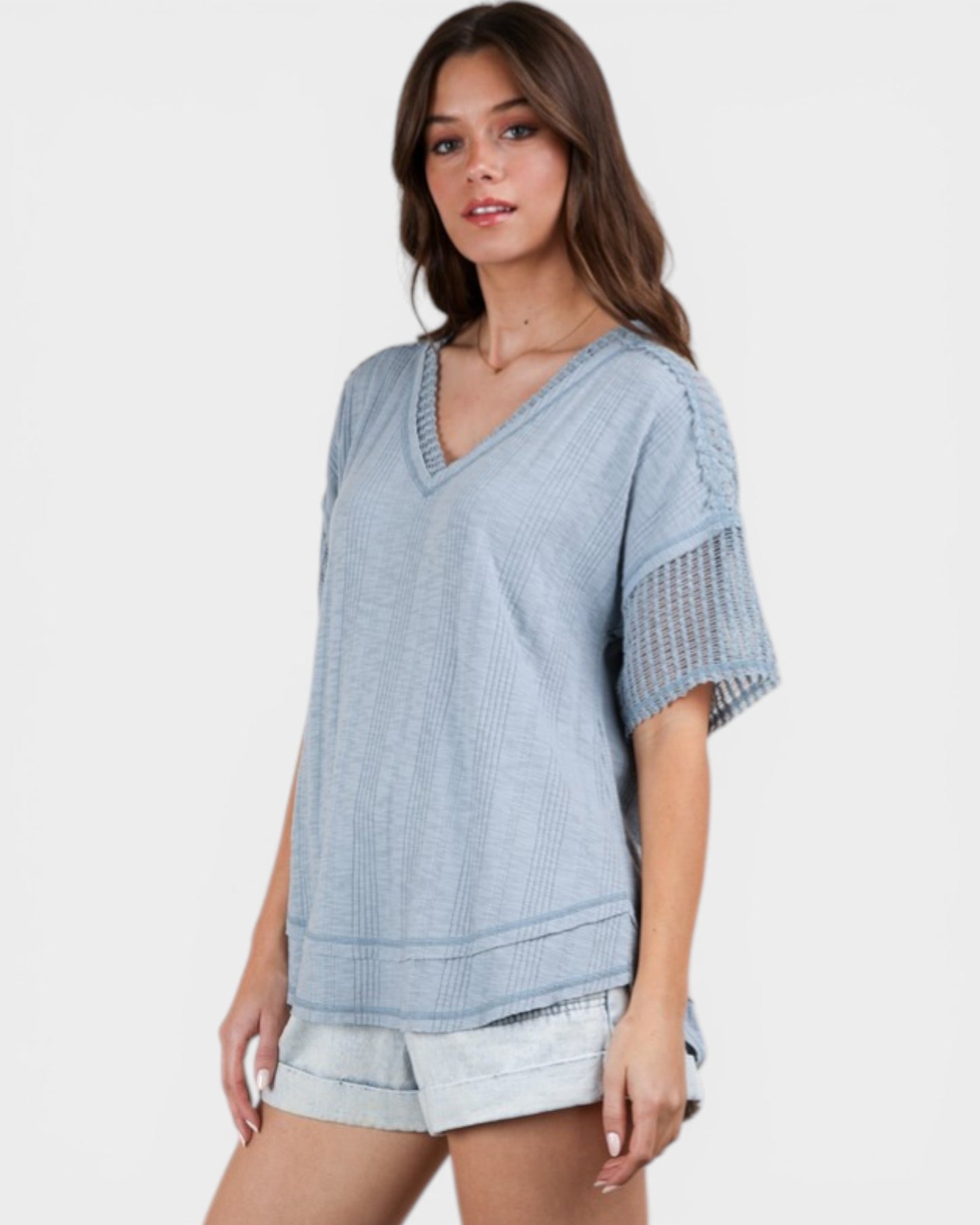 Woman wearing a light blue textured top and shorts on a white background